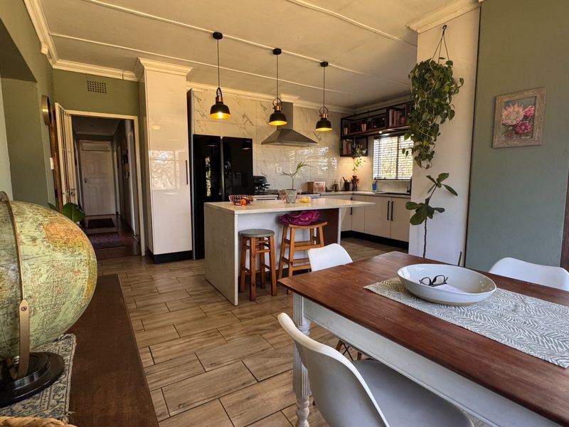 An open-plan kitchen and dining area featuring a central island, modern pendant lighting, tiled flooring, and direct access to an outdoor patio space.