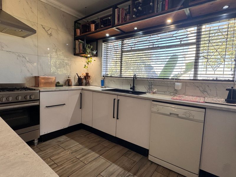 Modern kitchen featuring marble-look wall tiles, stainless steel gas stove, black fixtures, and ample built-in cabinetry with integrated dishwasher.