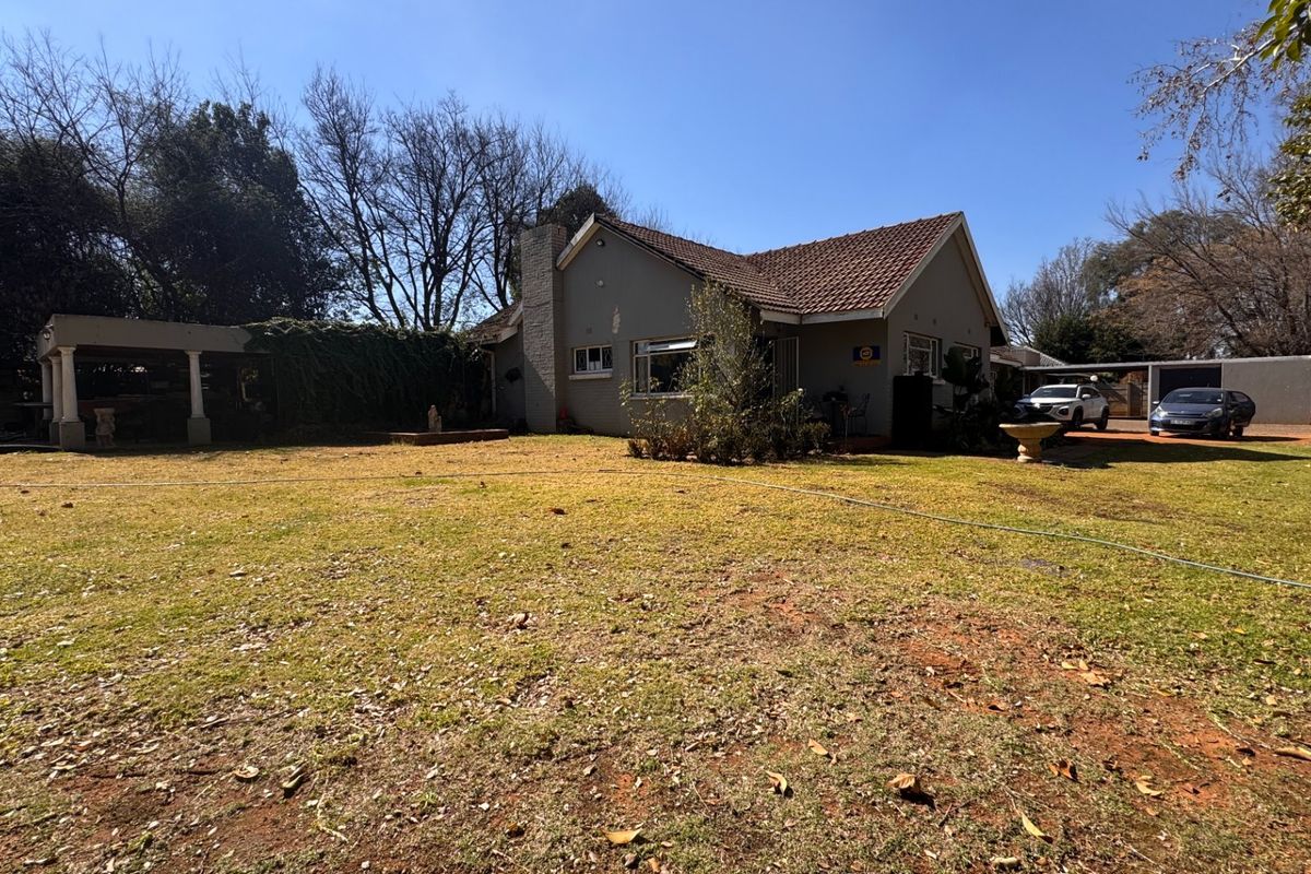 Rear view of the house featuring a tiled roof, brick chimney, and a covered patio area overlooking a large garden.