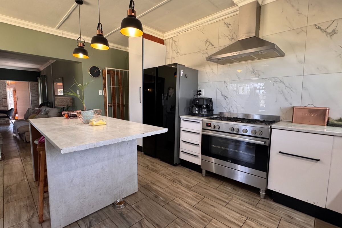 Modern kitchen featuring a central island, stainless steel gas stove with extractor fan, and elegant marble-look wall tiling.