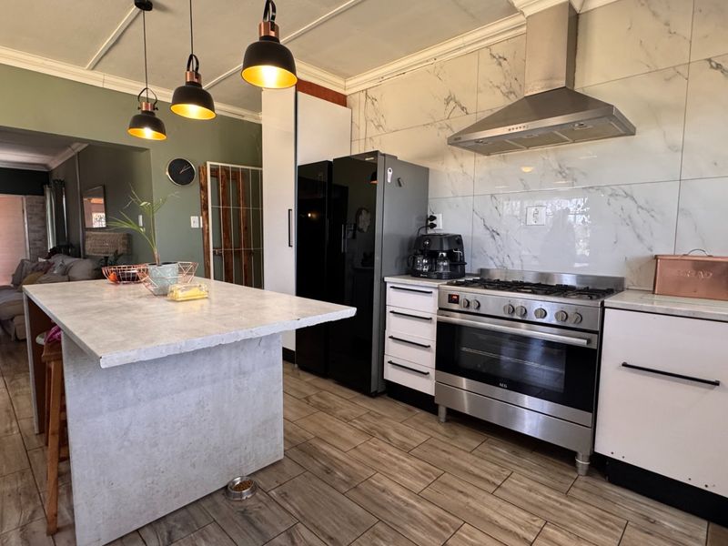 Modern kitchen featuring a central island, stainless steel gas stove with extractor fan, and elegant marble-look wall tiling.