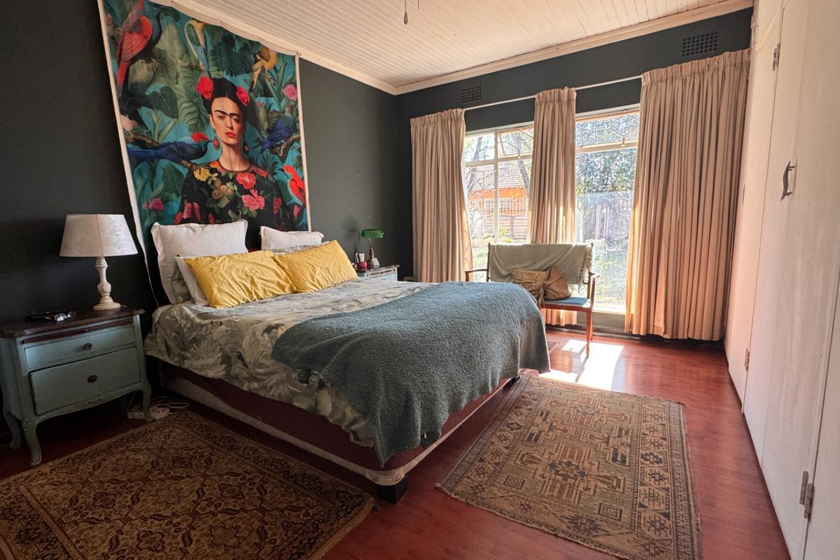 Spacious bedroom featuring timber flooring, a classic timber ceiling, and built-in cupboards, with large windows providing natural light.
