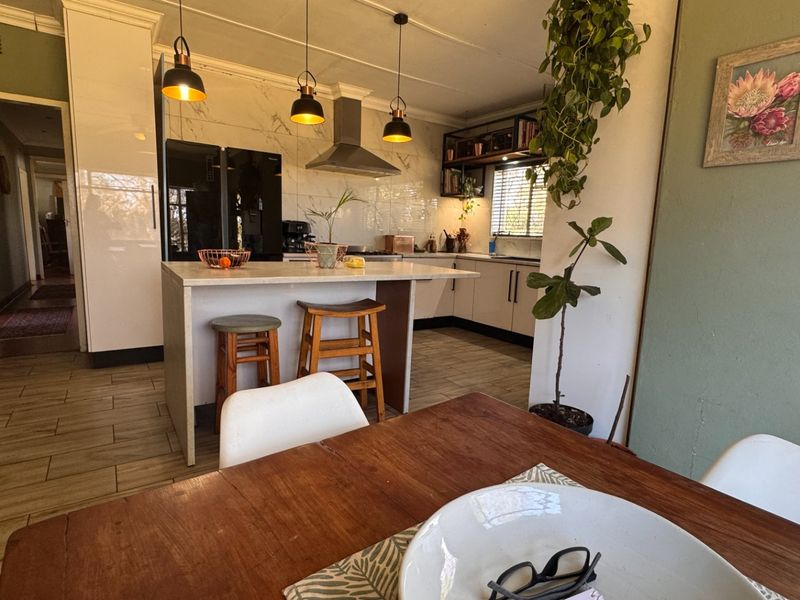 Open plan kitchen featuring a central island, modern cabinetry, stone countertops, and tiled flooring, seamlessly connecting to the dining area.