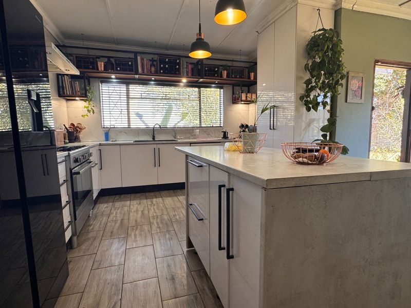 Modern kitchen featuring a central island, sleek white cabinetry, built-in oven with gas hob, and stylish pendant lighting over a functional workspace.