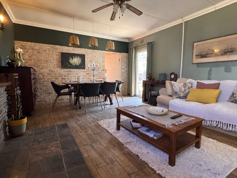 Spacious open-plan living and dining area featuring an exposed brick wall, tiled flooring, and a stone hearth, offering a warm and inviting atmosphere.