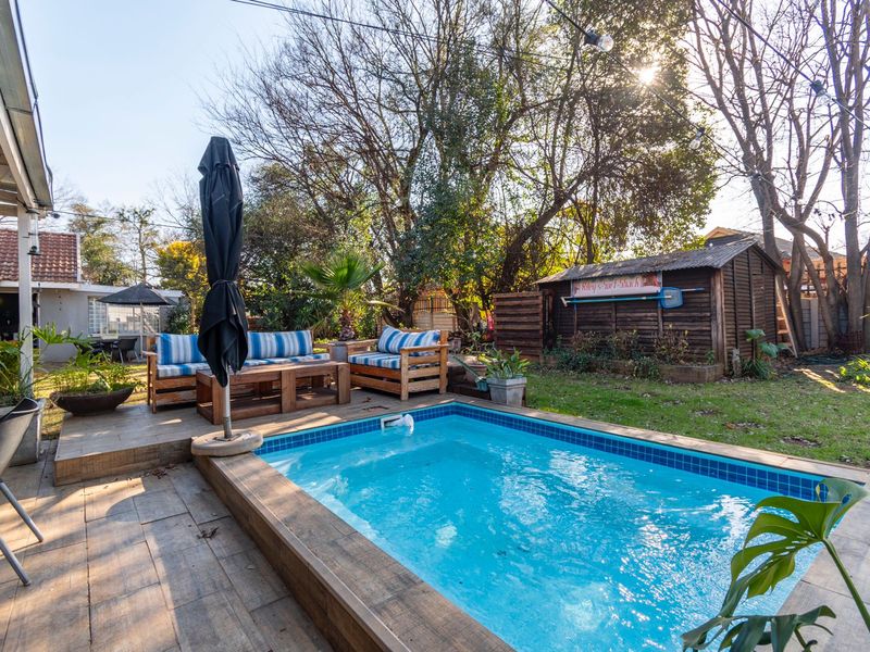 A well-maintained outdoor pool area featuring a tiled swimming pool, timber decking, and a wooden garden shed set within a landscaped backyard.