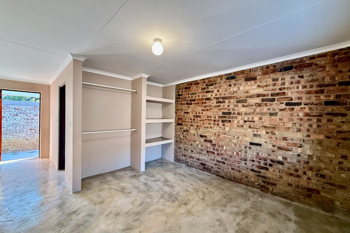 A bright bedroom featuring a rustic exposed brick wall, polished concrete floors, and built-in storage shelving and hanging rails.