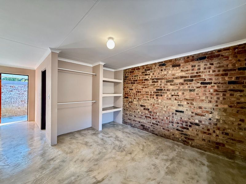 A bright bedroom featuring a rustic exposed brick wall, polished concrete floors, and built-in storage shelving and hanging rails.