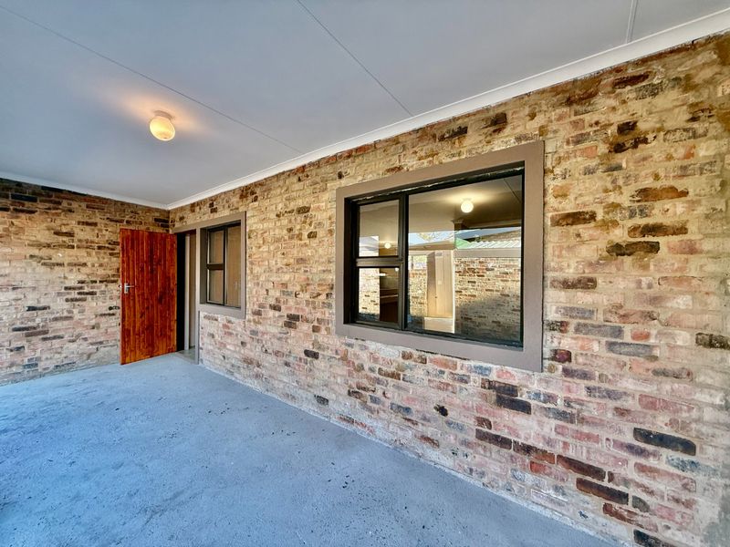 A covered patio area featuring exposed brick walls, concrete flooring, and aluminium-framed windows, providing a rustic outdoor space.