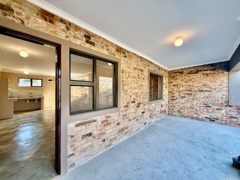 A covered patio area featuring exposed brick walls and concrete flooring, providing a rustic outdoor space with direct access to the interior living area.