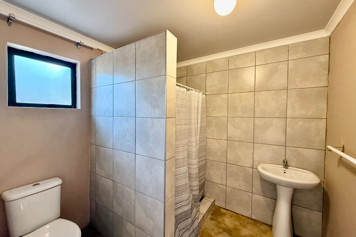 A functional bathroom featuring a pedestal basin, toilet, and a tiled shower area with a privacy partition.