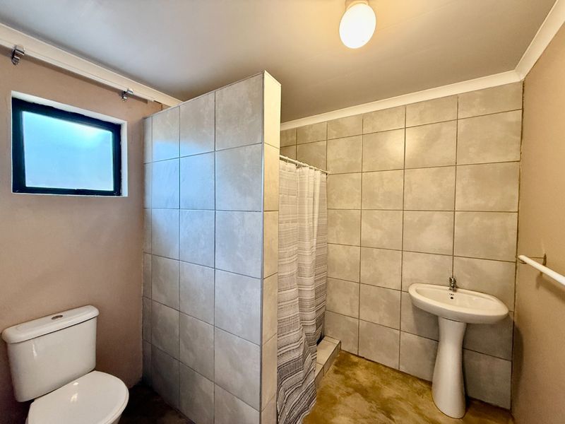 A functional bathroom featuring a pedestal basin, toilet, and a tiled shower area with a privacy partition.