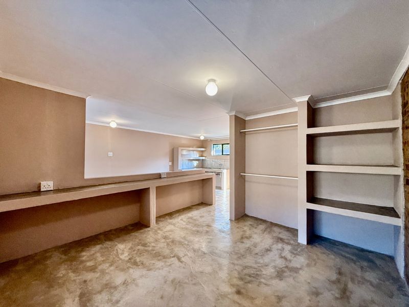 Open plan living area featuring polished concrete floors, built-in shelving, and a breakfast counter, leading through to a functional kitchen space.