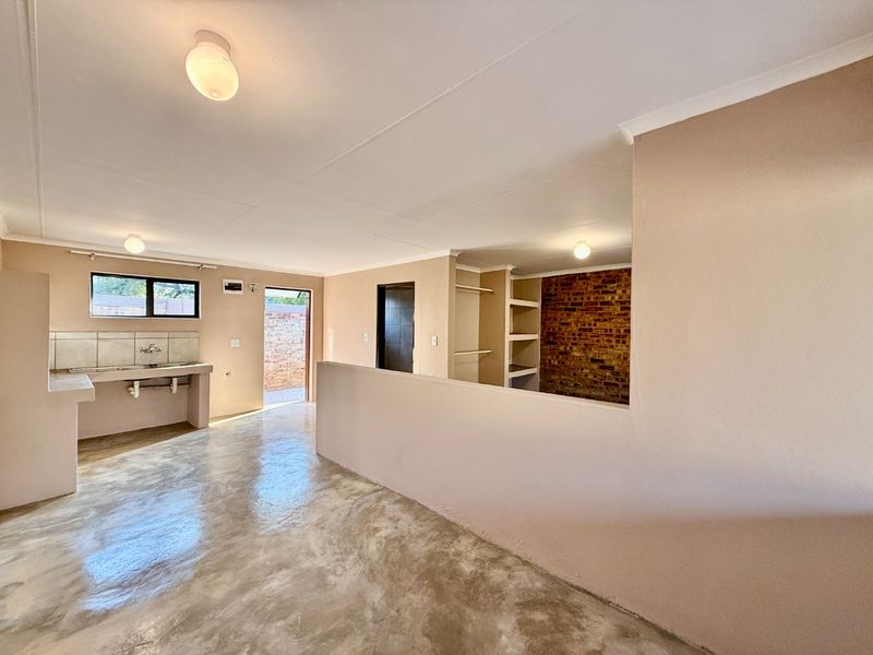 An open-plan living and kitchen area featuring polished concrete floors, exposed brick accents, and built-in shelving, offering a blank canvas for renovation.