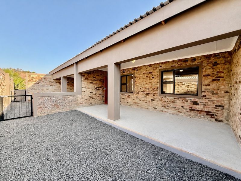 A clean, covered patio area featuring exposed brick walls, concrete flooring, and metal-framed windows, providing a functional outdoor space.