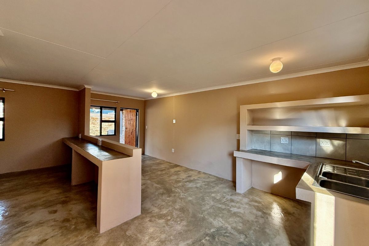 Open plan living and kitchen area featuring polished concrete flooring, built-in concrete cabinetry, and a breakfast bar in a minimalist, unfinished style.