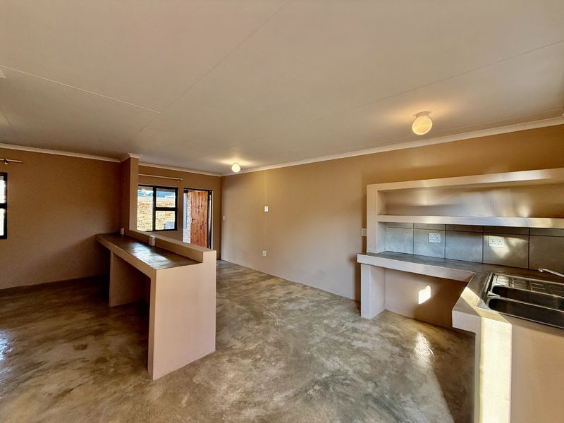 Open plan living and kitchen area featuring polished concrete flooring, built-in concrete cabinetry, and a breakfast bar in a minimalist, unfinished style.