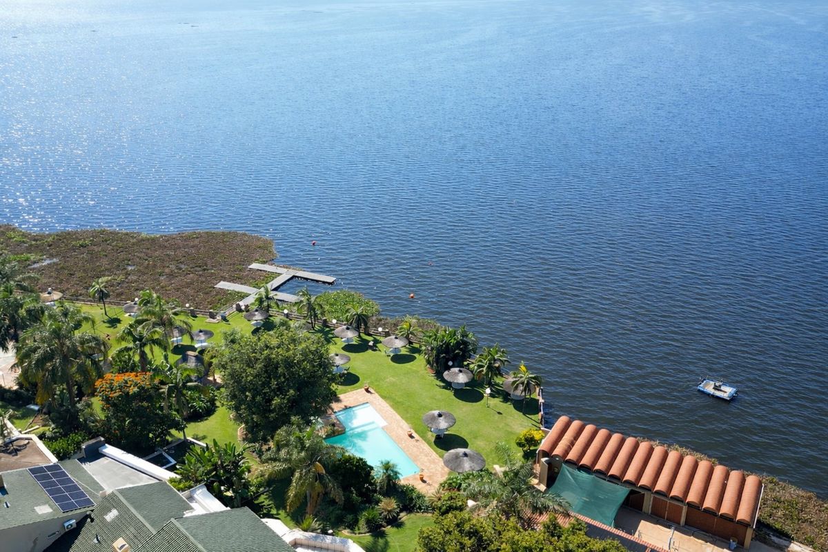 Aerial view of a waterfront property featuring a swimming pool, landscaped garden, private jetty, and solar panels on the main building roof.