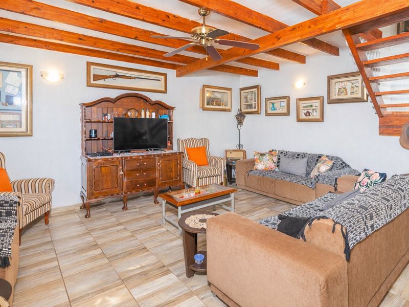 A living room featuring exposed timber ceiling beams, a ceiling fan, and tiled flooring, with an adjacent staircase leading to an upper level.