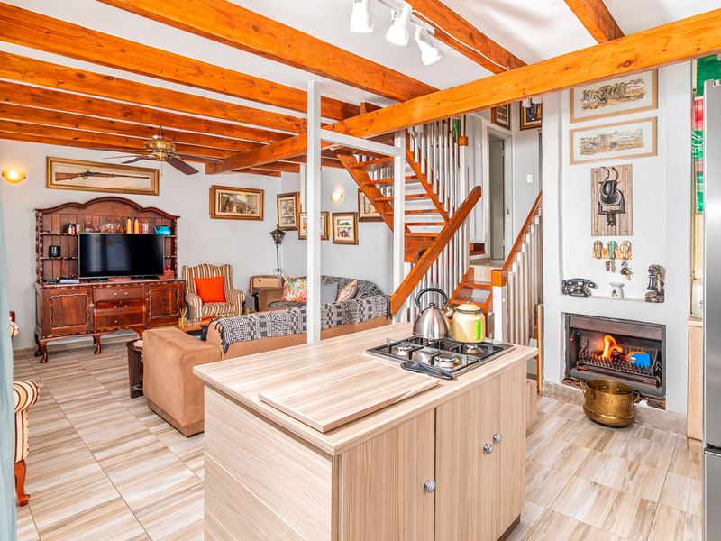 Open-plan living area featuring exposed timber beams, a built-in fireplace, a central kitchen island with a gas hob, and a timber staircase.