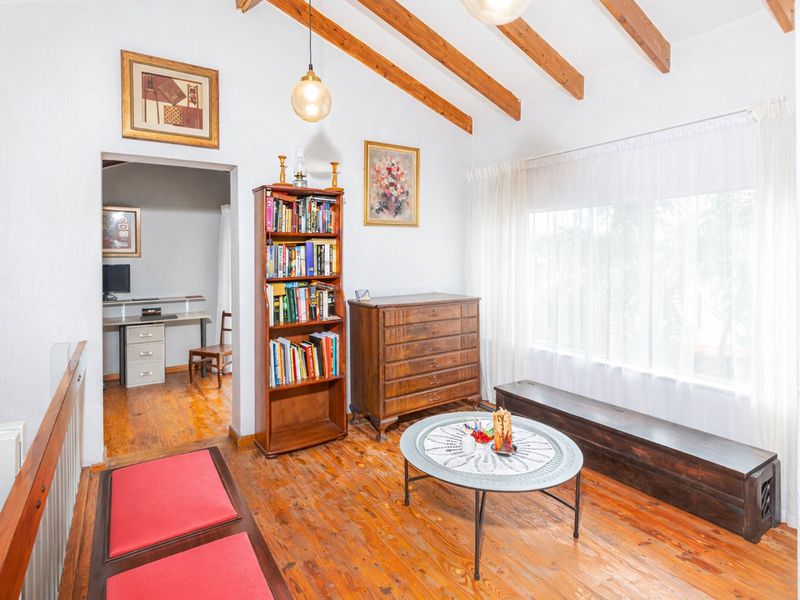 A cozy living area featuring exposed timber ceiling beams, warm timber flooring, and a staircase railing, creating a rustic and inviting atmosphere.