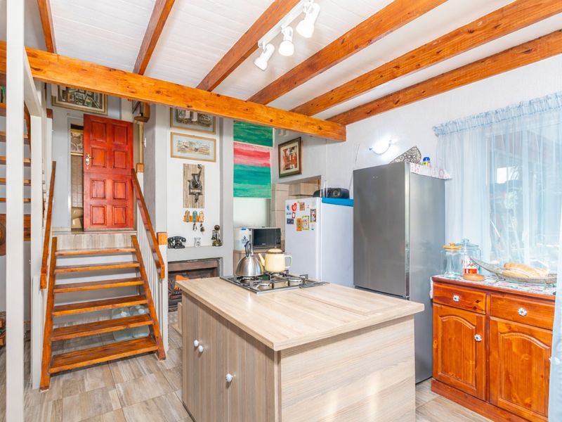 A rustic kitchen featuring exposed timber ceiling beams, a central island with a gas cooktop, and an integrated staircase leading to an upper level.