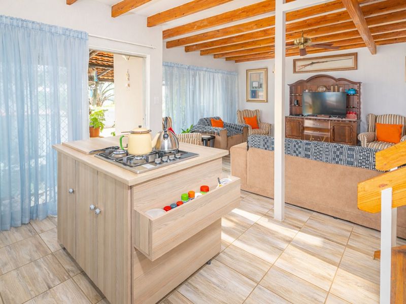Open plan living area featuring exposed timber ceiling beams, tiled flooring, and a central kitchen island with a built-in gas hob.