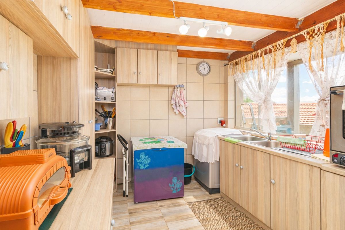A functional kitchen featuring laminate cabinetry, a double bowl stainless steel sink, tiled splashback, and exposed timber ceiling beams.