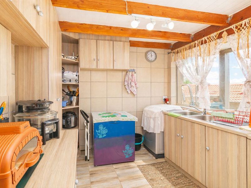 A functional kitchen featuring laminate cabinetry, a double bowl stainless steel sink, tiled splashback, and exposed timber ceiling beams.