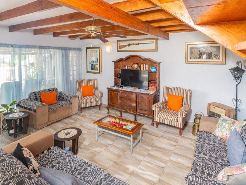 A living room featuring exposed timber ceiling beams, a ceiling fan, and ceramic floor tiles, with an adjacent staircase leading to an upper level.