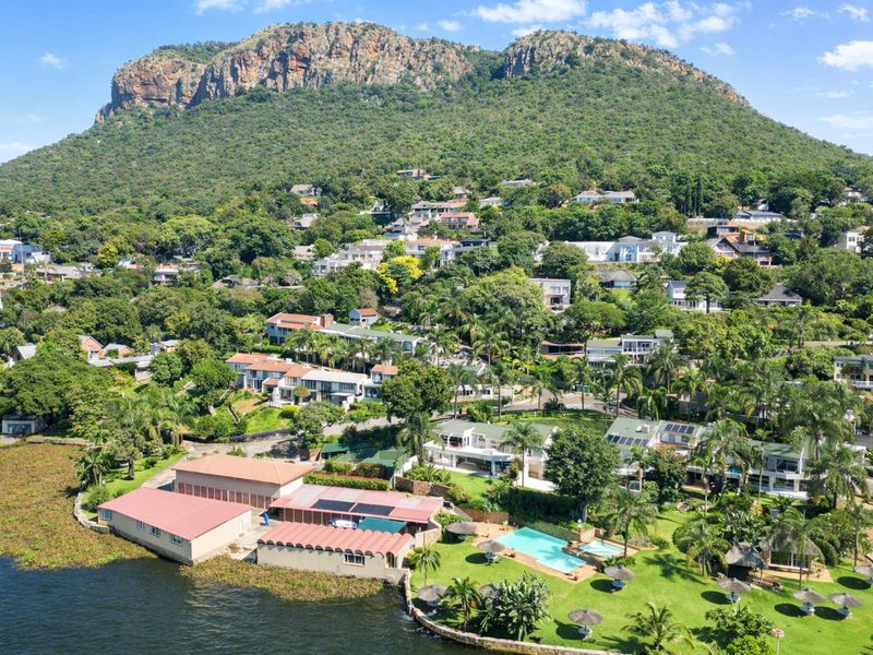 Aerial view of a residential estate featuring a swimming pool, landscaped gardens, and solar installations, set against a prominent mountain backdrop.