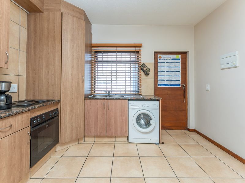 Functional kitchen featuring wood-look cabinetry, laminate countertops, built-in oven, hob, and tiled flooring with direct access to an exterior door.