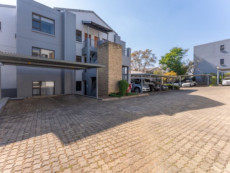 Exterior view of the townhouse complex featuring paved driveway, covered parking bays, and multi-story building facade.