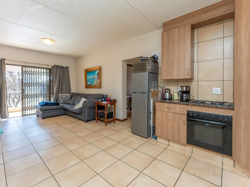 Open-plan living area featuring tiled flooring, a compact kitchen with built-in cabinetry, and a sliding door leading to an outdoor balcony.