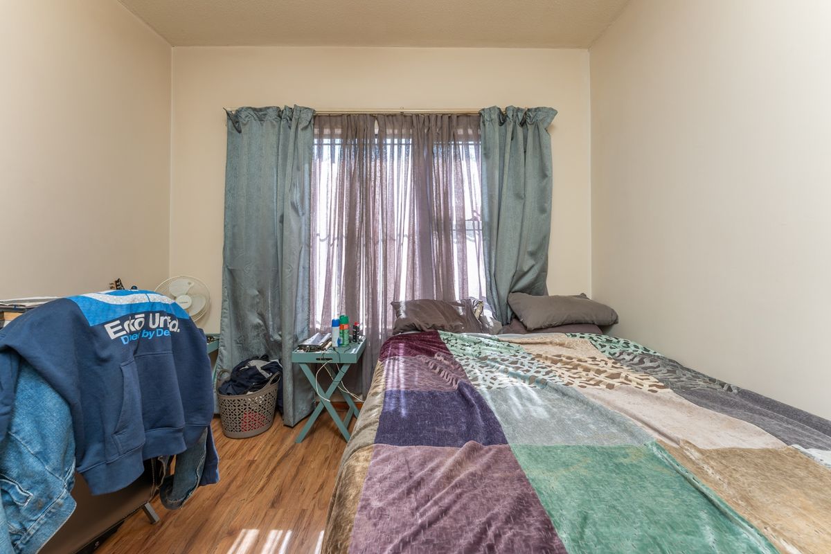 A standard bedroom featuring laminate flooring and a window with installed curtain tracks, providing a functional living space.