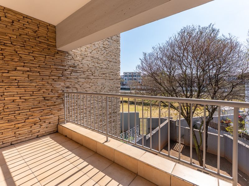 A covered balcony featuring a decorative stone-clad feature wall, tiled flooring, and a metal balustrade overlooking the surrounding grounds.