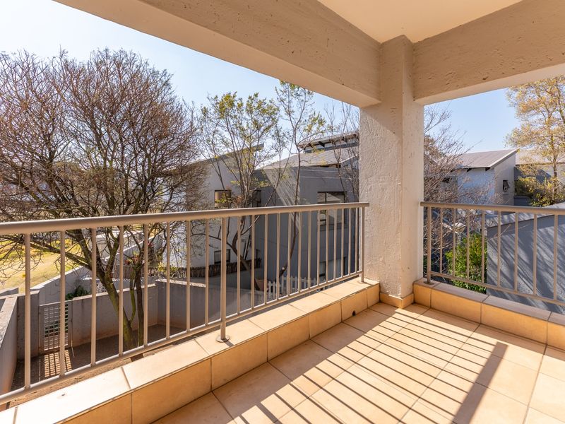 A covered balcony featuring tiled flooring and a metal balustrade, offering an open view of the surrounding townhouse complex.