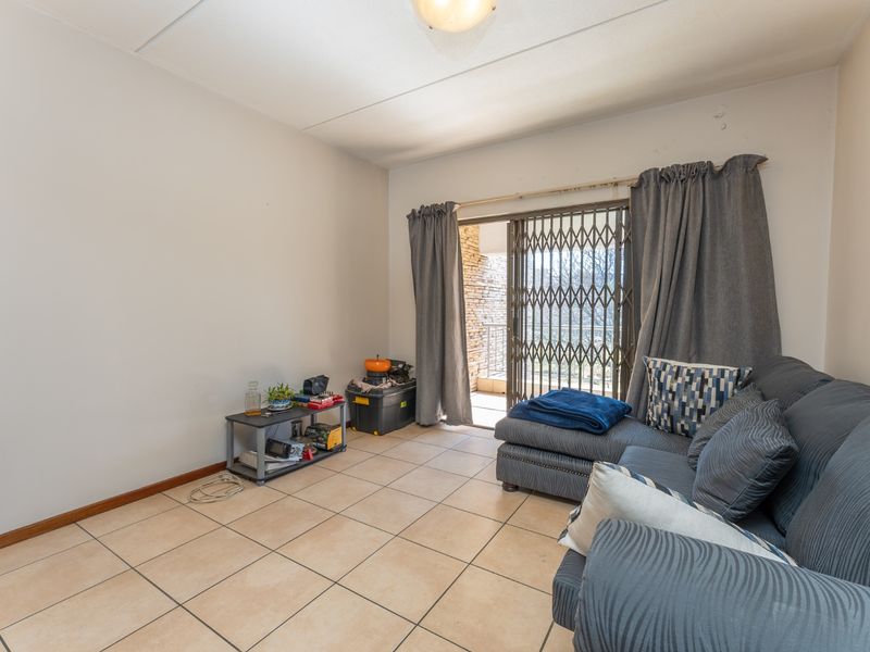 A living room featuring ceramic floor tiles and a sliding glass door with a security gate, providing access to an outdoor area.