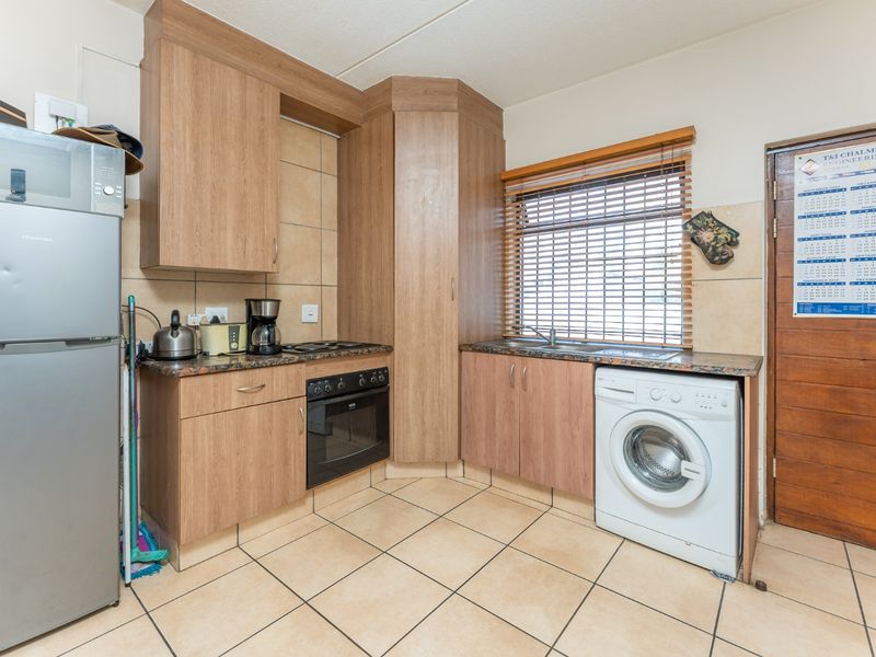 A functional kitchen featuring laminate cabinetry, granite countertops, built-in oven, electric hob, and tiled flooring with a dedicated space for a washing machine.