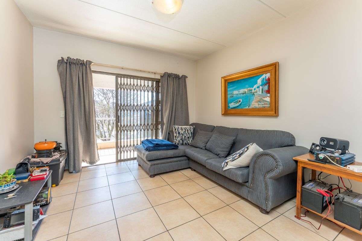 A living room featuring tiled flooring and a sliding glass door with a security gate, providing access to an outdoor balcony area.