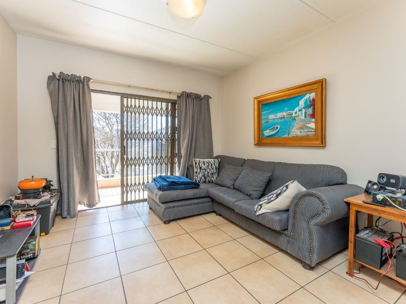 A living room featuring tiled flooring and a sliding glass door with a security gate, providing access to an outdoor balcony area.