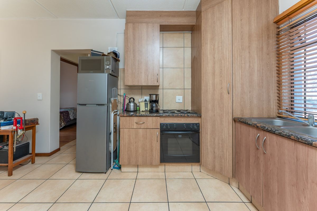 Compact kitchen featuring laminate cabinetry, granite countertops, built-in oven, electric hob, and tiled flooring, offering a functional and efficient workspace.