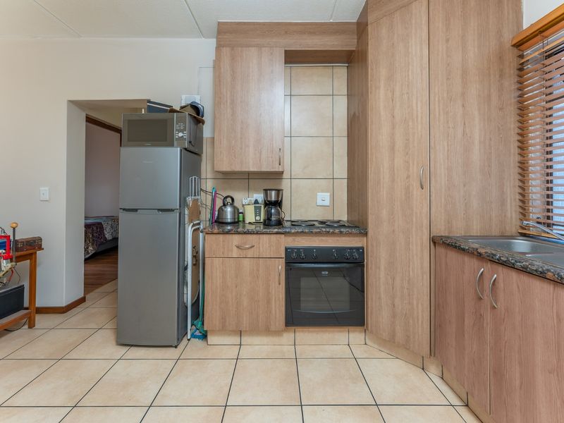 Compact kitchen featuring laminate cabinetry, granite countertops, built-in oven, electric hob, and tiled flooring, offering a functional and efficient workspace.