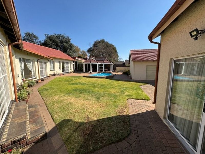 Spacious rear garden featuring a central lawn, paved walkways, a swimming pool, and a detached gazebo, surrounded by the main house and garage.
