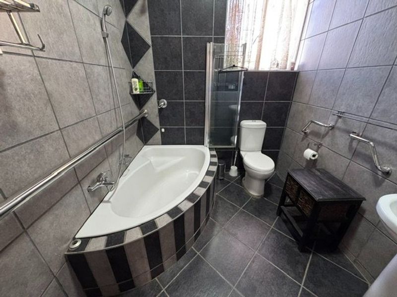A modern bathroom featuring a corner bathtub with handheld shower, toilet, and tiled finishes with safety grab rails installed.