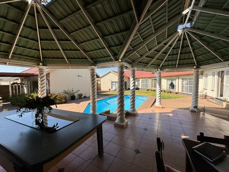 Spacious covered patio area featuring decorative columns, tiled flooring, and direct access to an outdoor swimming pool and garden.