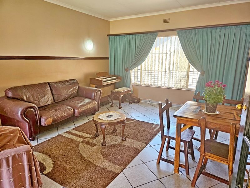 Open-plan living and dining area featuring ceramic floor tiles, large windows with security bars, and neutral wall finishes.