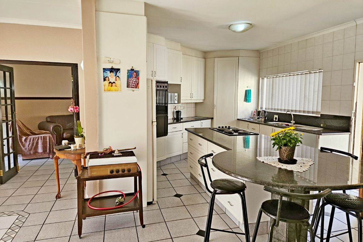 A functional kitchen featuring white cabinetry, granite countertops, a central island with a gas hob, and tiled flooring throughout.