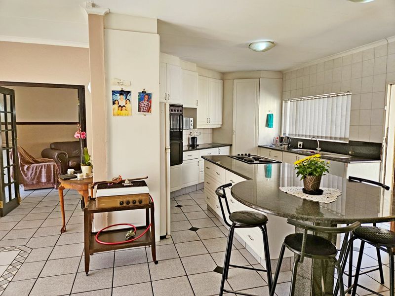 A functional kitchen featuring white cabinetry, granite countertops, a central island with a gas hob, and tiled flooring throughout.