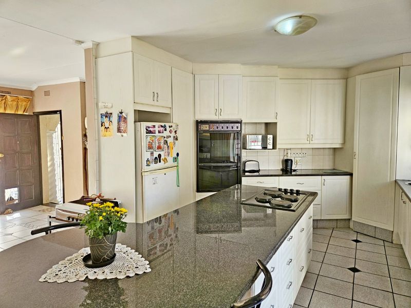A functional kitchen featuring granite countertops, built-in oven and hob, and white cabinetry, with tiled flooring throughout.